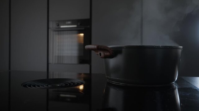 Close up of a sleek induction cooktop with an integrated downdraft ventilation system suctioning steam from a black pot in a minimalist kitchen.
