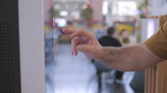 Hand taps on glass screen in modern office. Background shows blurred coworkers. Action suggests digital interaction or touchscreen use. Suitable for tech, workplace, or interface projects