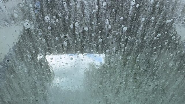 A view through the front window of a car going through an automatic car wash machine with Spinning brushes, water and soap suds.