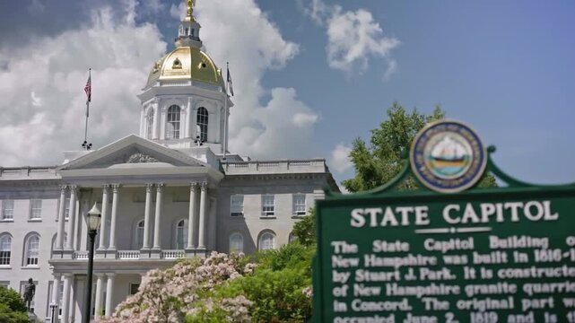 Static cinematic view of the New Hampshire State House sign with the historic capitol building entrance in the background in Concord New Hampshire on a clear summer day.