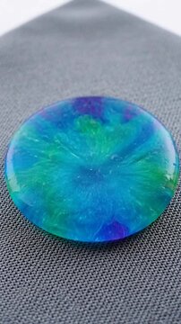 Polished round iridescent opal gemstone with vibrant blue and green colors.
