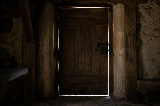 A heavy oak door closed with bright light outside and deep shadows.