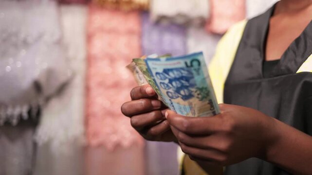 African woman small business owner counting money, showing financial success in her textile shop