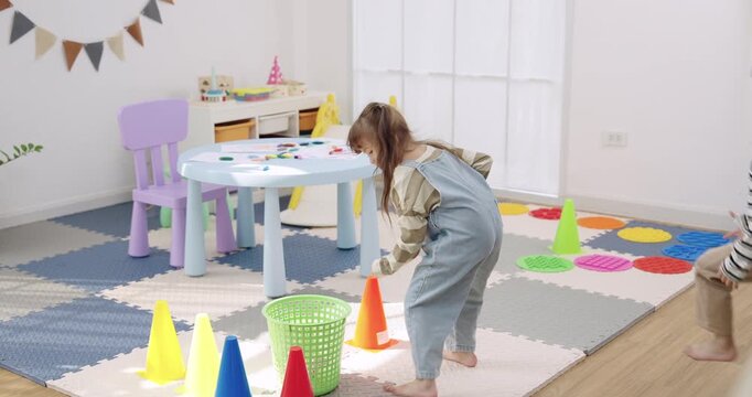 Asian son watches preschool daughter pick cone, drop item into basket, siblings share turn, learn rule, cooperation, patience, laughter, supportive single mother nearby, slow motion indoor activity.