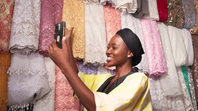 African woman small business owner recording content for social media at her textile shop