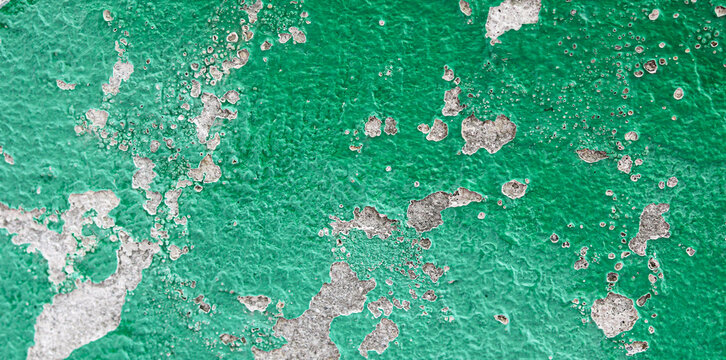 Wide-angle shot of a weathered concrete surface coated in a layer of textured emerald green paint. It displays heavy weathering and age, with the green paint chipping, flaking, and peeling away.
