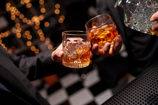 Close-up shot of a businessman clinking a glass of whiskey with ice in a bar at night.
