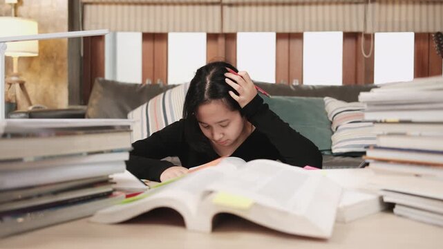 College Asian teenage girl tired and burned out from overwhelmed study pile of books, stressed learning at home with stack of textbooks, reading and writing for school exam, homeschooling education.