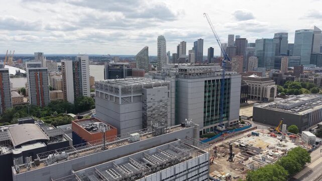 Aerial perspective over a large data center complex in London's Canary Wharf. Observe ongoing city development and construction near the River Thames. Bright daytime sky with clouds.