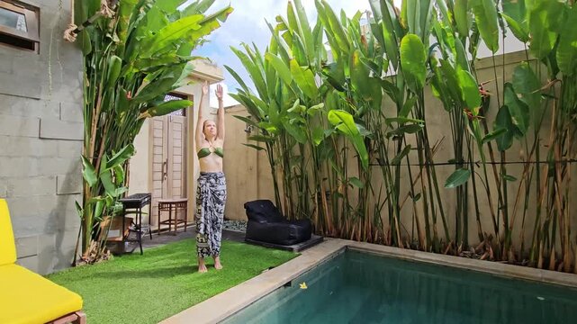 Camera panning over a lady practicing morning yoga and breathing exercises in a lush green garden in Bali, Indonesia. Peaceful mindfulness concept.