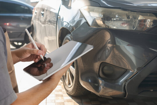 Insurance agent using tablet inspecting damaged car.