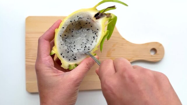 Hands Scooping White Flesh From Halved Yellow Dragon Fruit With Spoon