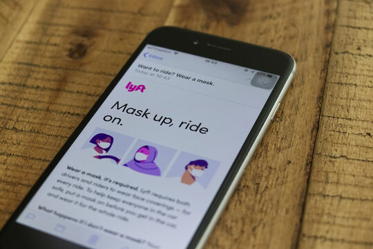 A smartphone on a wooden table shows a Lyft email reading Mask up, ride on, requiring drivers and riders to wear face masks during the COVID-19 pandemic.