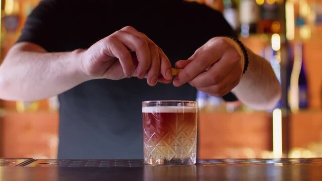 Drink presentation. Alcohol beverage. Unrecognizable professional male barman hands serving decoration with lemon spiral zest cherry on bar counter.