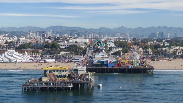 Santa Monica, California, USA - JANUARY 05, 2025: Aerial view of Santa Monica Pier featuring colorful ferris wheel and amusement park with beach cityscape and mountains in background.