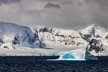 Vividly colored blue iceberg floating in the Southern Sea near the ice sheet of the Antarctic Peninsula. Dark, cloudy sky in the background.   © dhayes