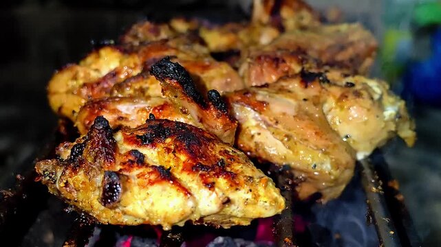 Close-up of marinated chicken pieces grilled on a charcoal barbecue with glowing embers at night. 4K