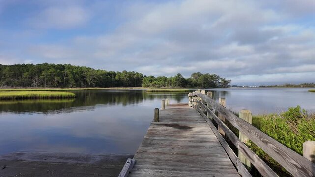 Scenic footage of a peaceful coastal river with a wooden pier extending into calm tidal waters, capturing the beauty of a quiet waterfront landscape.