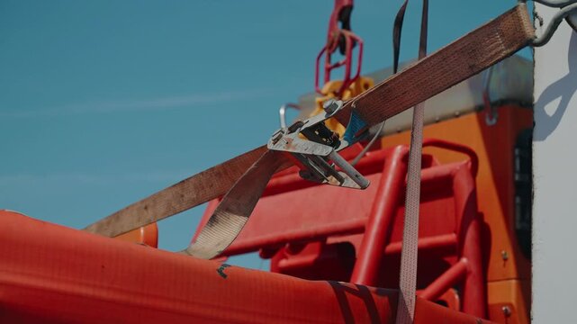 Ratchet Strap And Buckle Lashing Orange Life Raft Container On Ferry Deck Under Blue Sky