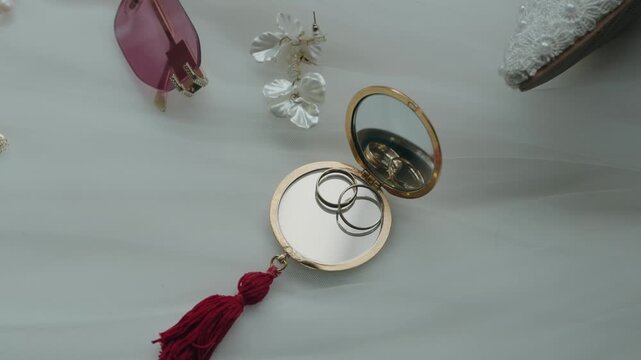 Two Gold Wedding Rings In Round Compact Mirror Beside Earrings And Sunglasses Flat Lay