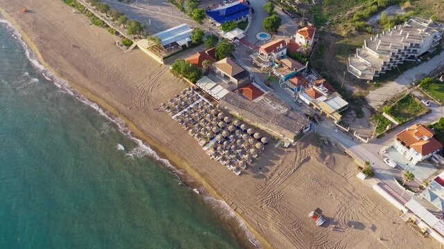 Drone of Kourouta Beach with beachfront buildings and organized umbrellas, aerial medium orbit before tourists come out