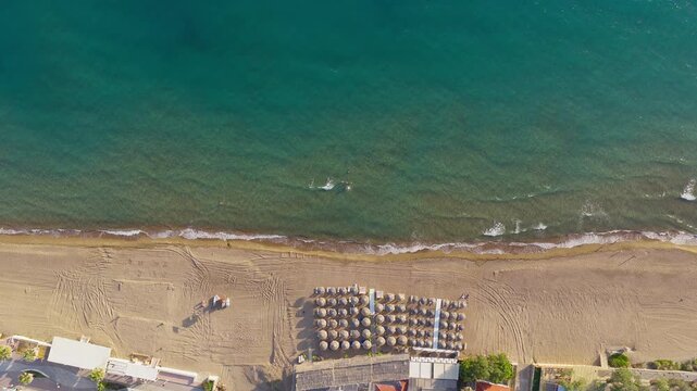 Top down drone of Kourouta Beach shoreline with umbrellas and turquoise sea, aerial tracking left at sunrise