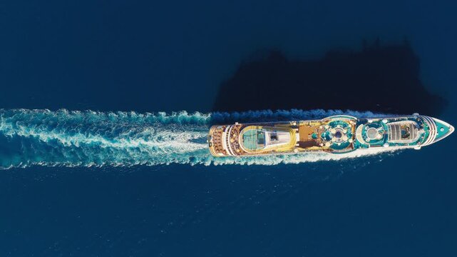 Cruise ship sailing through open sea with long white wake, aerial top down backdrop with stunning shadow and vacation textured decks with pools