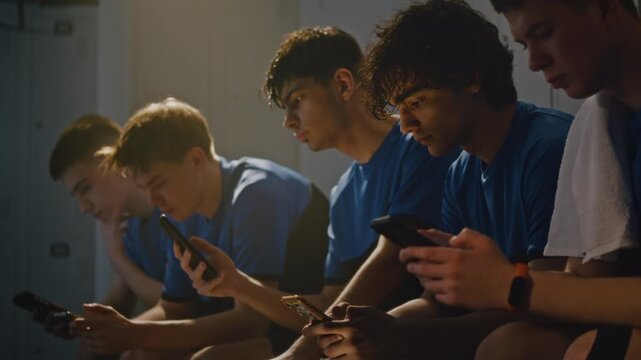 Youth Boys in Sports Uniforms Sitting on Locker Room Bench. Teenager Absorbed in Own Mobile Phone, Scrolling Through Social Media or Apps Before Training. Modern Technology Addiction, Screen Time.
