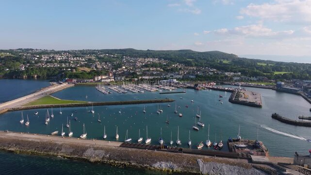Sailboats fill the marina and outer moorings at Howth as a drone glides above the harbour walls and coastal town.