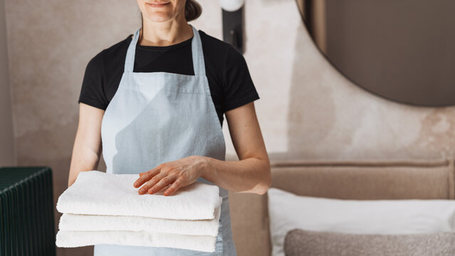 Maid holds fresh folded towels in hotel room for guests enjoying their stay