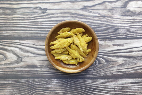 A close-up view of a group of fried rasboras in a wooden saucer on a wooden table. Fried rasboras, commonly known as wader goreng in Indonesia, are a popular, crispy local delicacy.