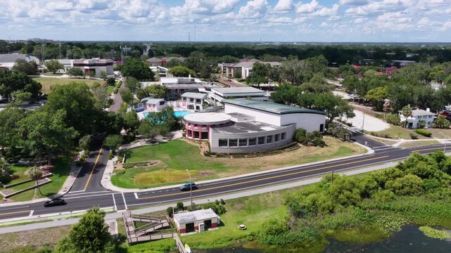 Frank Lloyd Wright curved building overlooks lake, wooden boat dock house, tree-lined road, scattered clouds, Florida Southern College campus, Lakeland, Florida, USA. Aerial drone wide shot