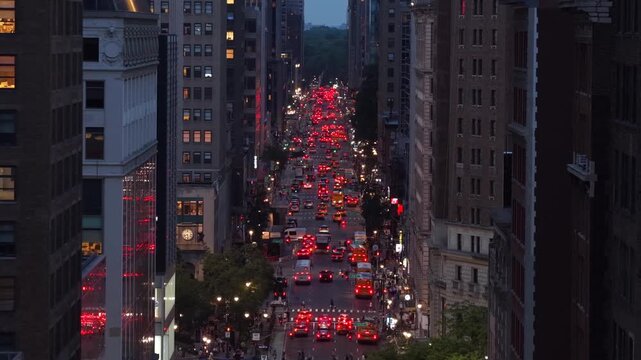 New York City avenue congested with rush hour traffic, red brake lights streaming through Manhattan skyscrapers at dusk, evening cityscape glowing amid dense urban towers. Aerial drone zoom shot