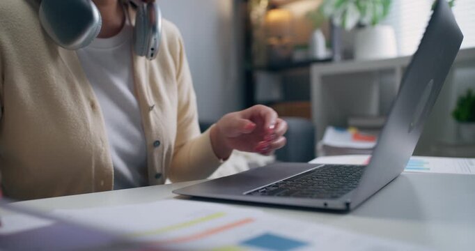 Close-up of Asian female financial analyst hands holding paper document and using laptop during remote work from home.