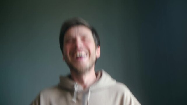 Happy caucasian man wearing hoodie celebrating success, joyfully laughing with excitement against solid dark grey background, expressing pure happiness, positive emotions. Man laughing with happiness