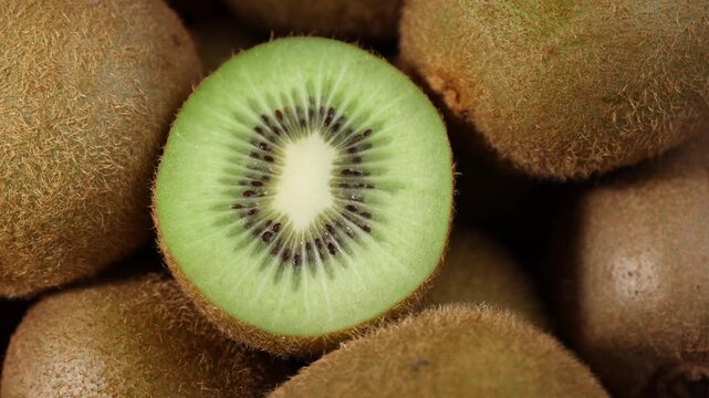 Close-up of fresh kiwi fruits arranged on a wooden table. Whole and sliced kiwis showing their vibrant green flesh and tiny black seeds under natural light. Ideal for themes of healthy eating, fresh f