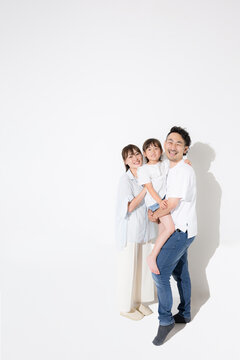 白背景で仲良し笑顔の家族・幸せなファミリーライフと健康的な暮らし　保険やnisaなど教育や成長、寄り添う抱っこの全身　広角のコピースぺースあり半袖夏イメージ