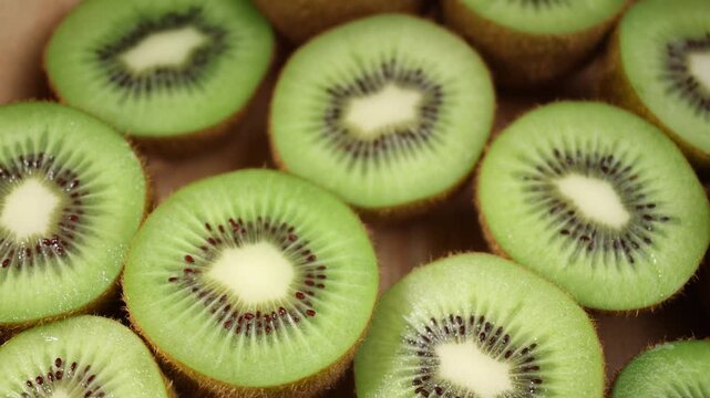 Close-up of fresh kiwi fruits arranged on a wooden table. Whole and sliced kiwis showing their vibrant green flesh and tiny black seeds under natural light. Ideal for themes of healthy eating, fresh f