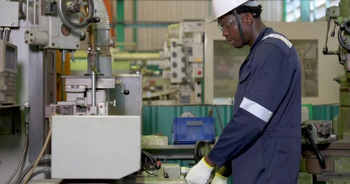 african adult male operator guides machine table by handwheel, monitors cutting setup in workshop, safety PPE workflow and precision equipment control support production task