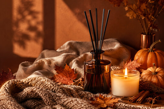 Aromatherapy reed diffuser with candle pumpkins maple leaves knitted blanket and cinnamon sticks creating warm autumn spa mood for cozy home fragrance ritual