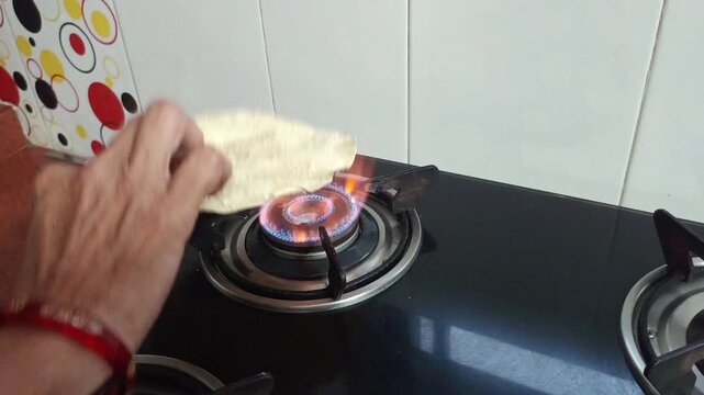 Indian woman roasting traditional papadum on a gas stove burner in a kitchen, close up