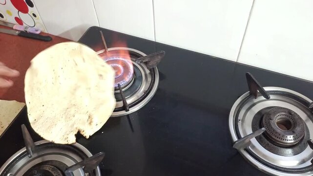 Indian woman roasting traditional papadum on a gas stove burner in a kitchen, close up