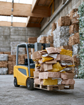 Yellow forklift moves crates in warehouse space. Stacks of bales line concrete walls behind. High ceilings and skylights let natural light stream. No workers are visible, so emotions are irrelevant