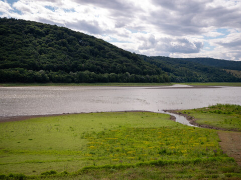 Low water level at Doma&scaron;a reservoir during drought. Exposed lakebed covered with grass and a small inflow near Petejovce, showing the effects of dry weather.
