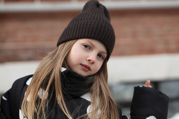 Portrait of a cute preteen girl in a brown knitted beanie hat looking directly at the camera outdoors. © Irina