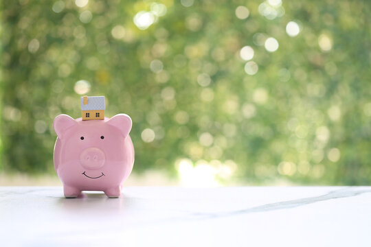 Miniature house model on a pink piggy bank, symbolizing financial savings for real estate, home purchase goals and future investment planning.