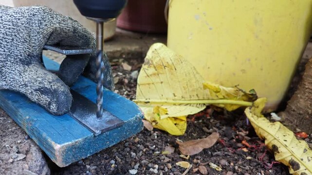 Gloved hand securely holding a steel flat bar while being drilled