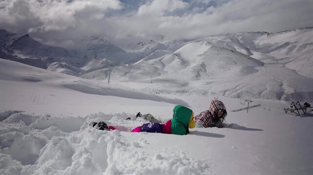 Girl throws snow while her mother falls laughing into deep powder at Las Le&ntilde;as Ski Resort in the Andes Mountains, Mendoza, Argentina, capturing playful winter recreation, slow motion.