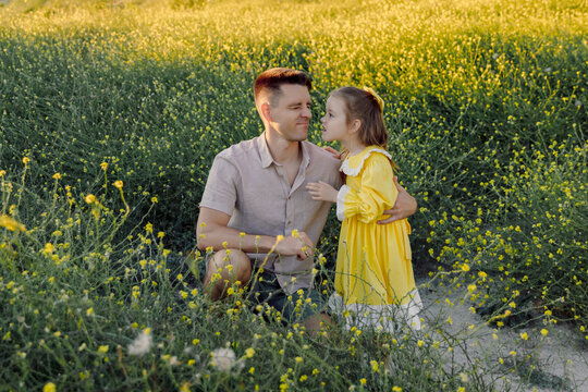 Father and daughter sitting and playing together in a meadow with sunlight.