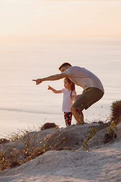 Father and daughter enjoying ocean view together on a sunny landscape during family trip.
